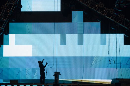 Side view of anonymous male worker silhouette setting up digital screen while looking up on stage