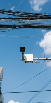 A surveillance camera mounted outdoors under a clear blue sky with power lines.